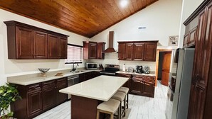 A kitchen with wooden cabinets, a large island with stools, a microwave, and a refrigerator. - Cozy 4-bedroom Cabin in Branson (Branson)