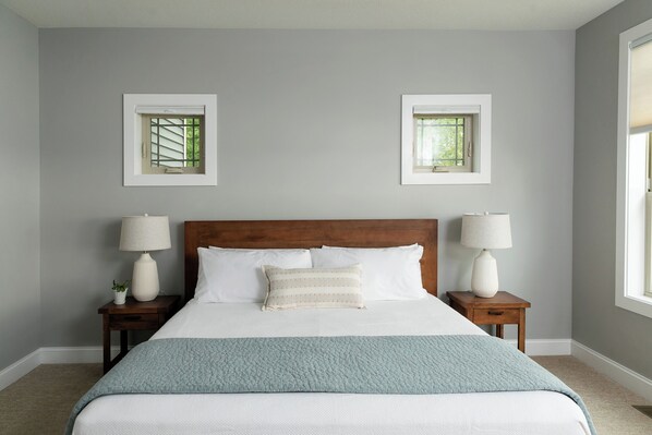 A neatly arranged bedroom with a large bed, two bedside tables with lamps, and two framed windows. - Spectacular Lakefront Retreat on Lake Michigan in Suttons Bay (Suttons Bay)