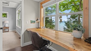 A room with a large window, a desk, a chair, a lamp, and a small table with a lamp.