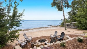 A beach setting with a fire pit and Adirondack chairs.