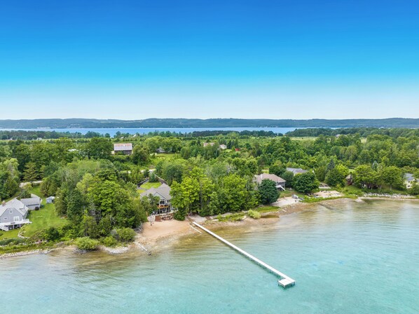 Vista aérea de una propiedad junto al lago con un muelle que se adentra en el agua, rodeada de exuberante vegetación y edificios residenciales.