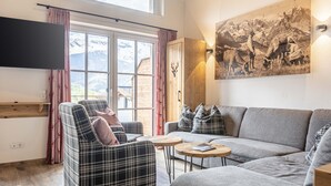 Una sala de estar moderna con sofá, sillón y mesa de centro. Un ventanal ofrece vistas a montañas.