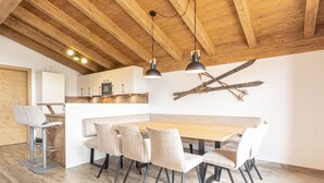 Una cocina moderna con vigas de madera, una zona de comedor con una mesa larga y sillas, y una decoración de pared con temática de esquí.