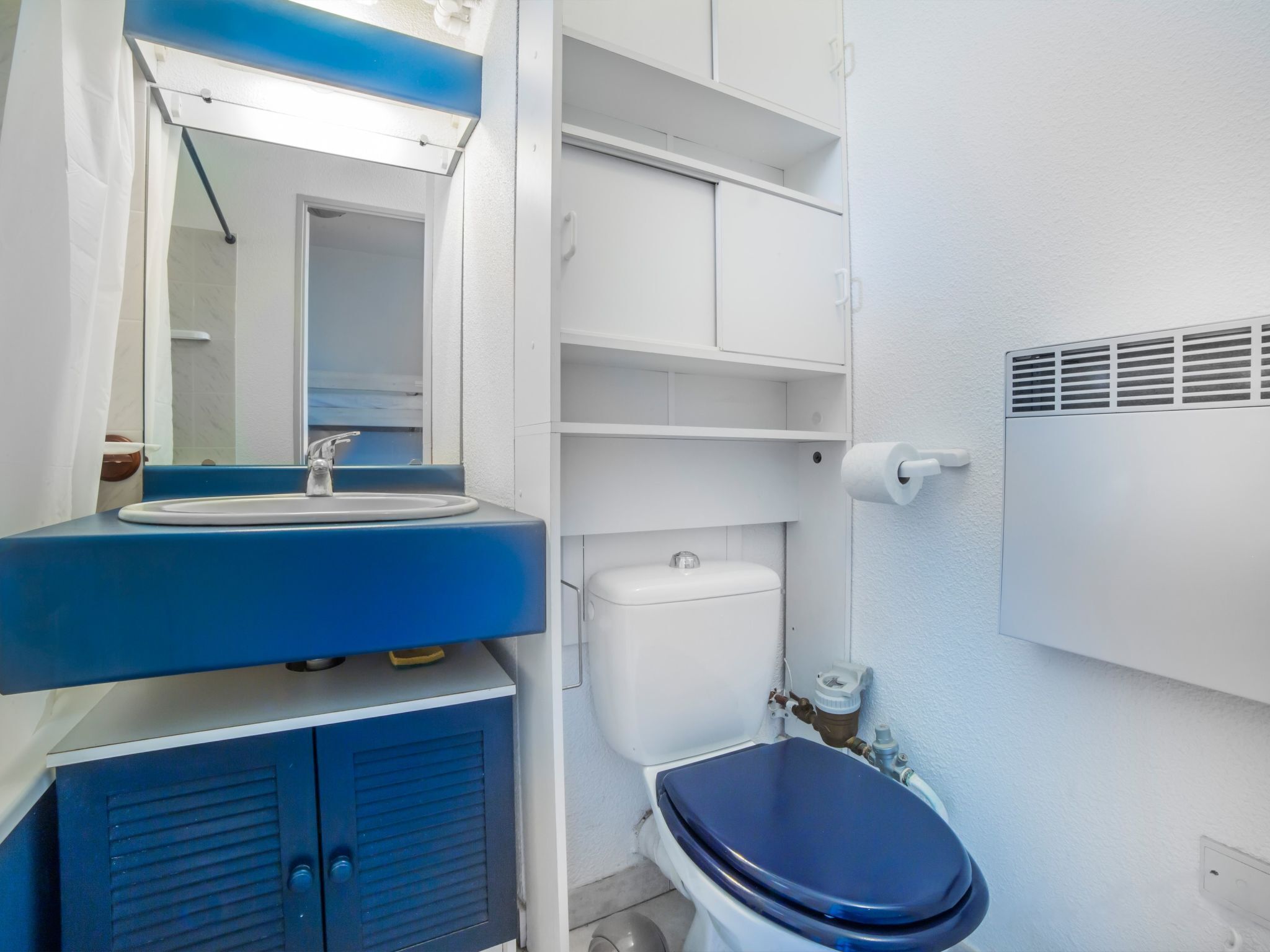 Une salle de bain avec un lavabo bleu, des toilettes blanches et un miroir au-dessus du lavabo.