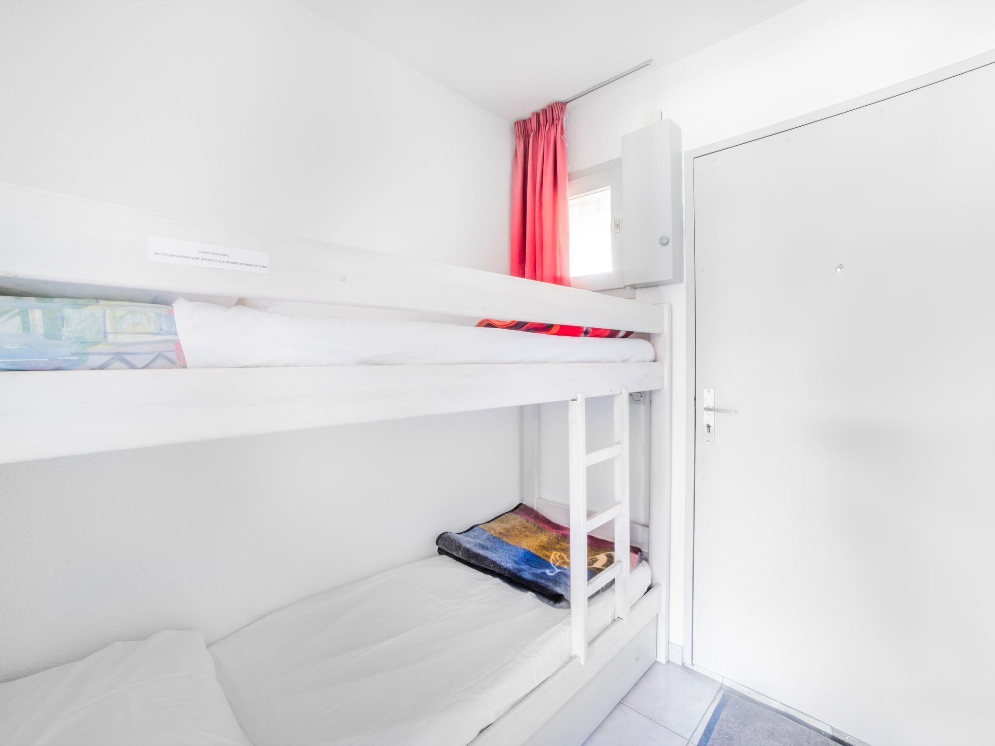 A bunk bed room with a white door and a window with red curtains.