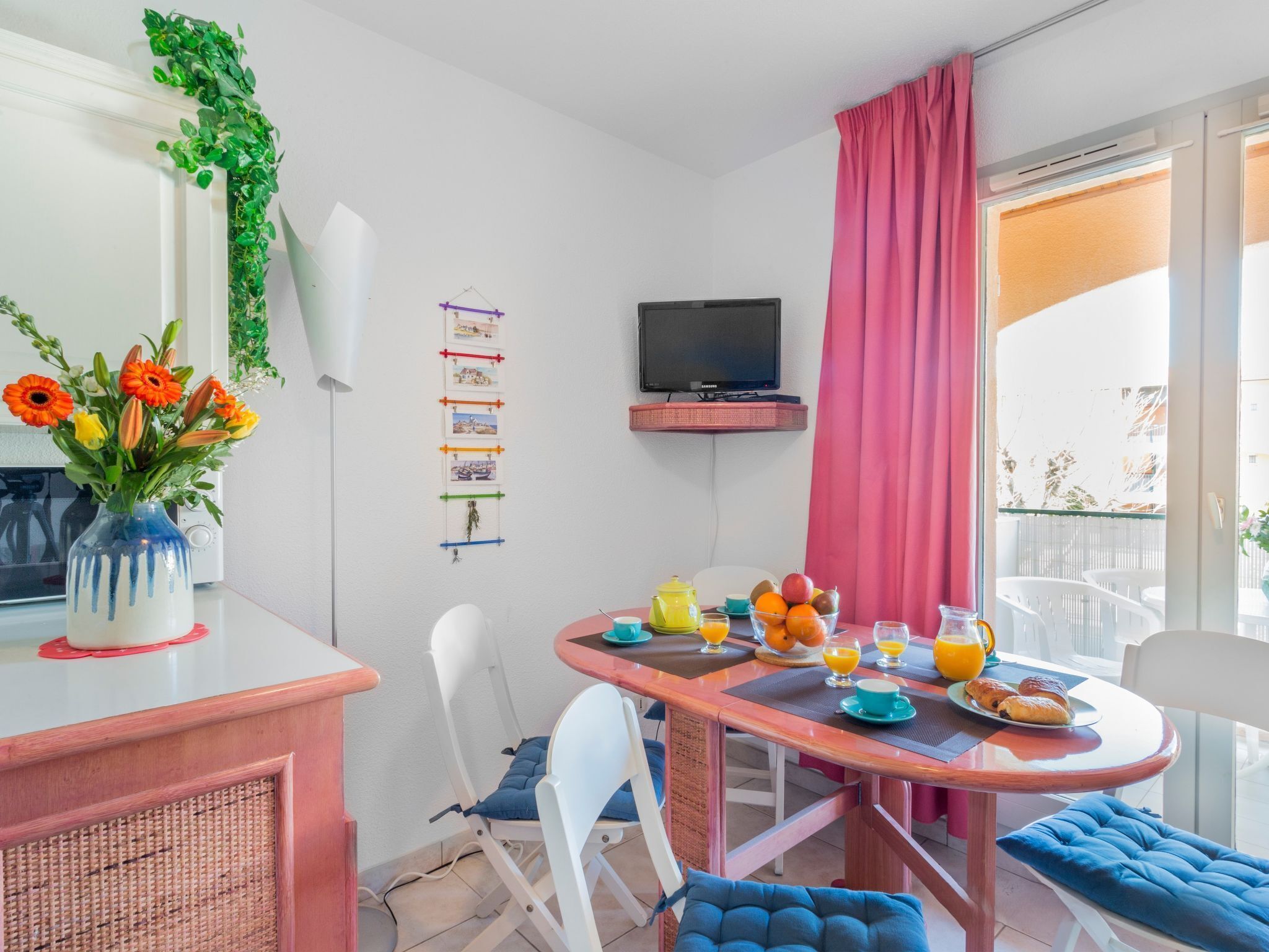 Ein Essbereich mit einem für das Frühstück gedeckten Tisch, einem an der Wand montierten Fernseher und einem Balkon mit Blick.