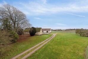 Un paysage rural avec une maison, un grand arbre et un champ dâherbe.