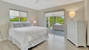 A bedroom with a bed, a ceiling fan, a dresser, and a window with a view of greenery. - Pristine 3-bedroom house with Heated Pool, WiFi and AC in lovely Marco Island (Marco Island)