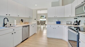 A modern kitchen with white cabinetry, a dishwasher, a stove, and a dining area with a table and chairs. - Pristine 3-bedroom house with Heated Pool, WiFi and AC in lovely Marco Island (Marco Island)