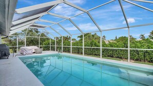 A swimming pool with a covered area, surrounded by greenery and a clear sky. - Pristine 3-bedroom house with Heated Pool, WiFi and AC in lovely Marco Island (Marco Island)