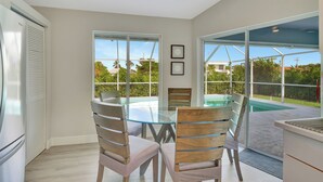 A modern kitchen with a glass dining table, wooden chairs, and a view of a swimming pool. - Pristine 3-bedroom house with Heated Pool, WiFi and AC in lovely Marco Island (Marco Island)