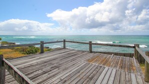 Eine Holzterrasse mit Blick auf eine Küstenlandschaft, das Meer und einen bewölkten Himmel.