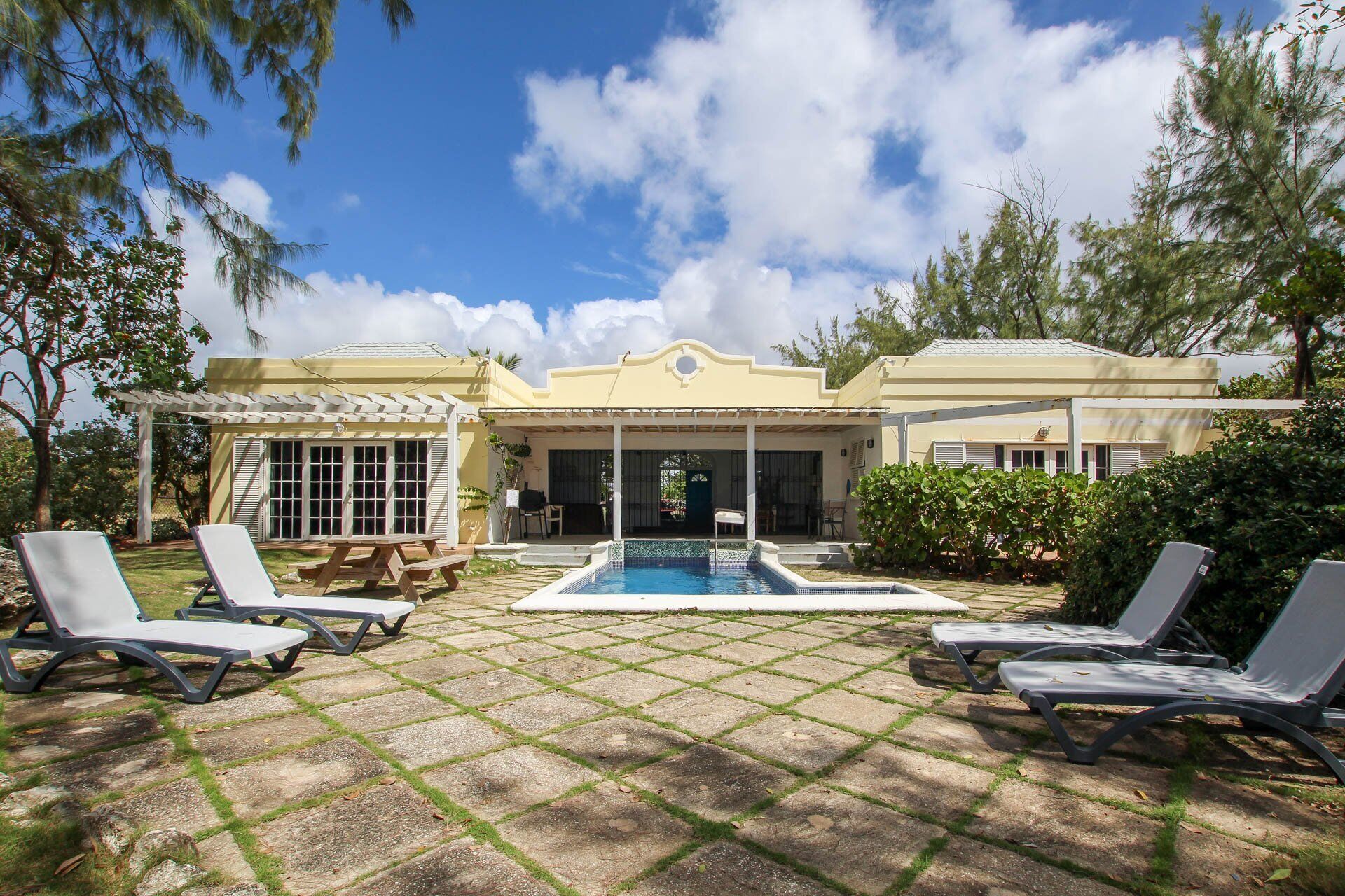 Une maison avec une piscine, un patio couvert et des chaises longues.