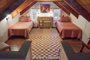 A cozy attic bedroom with two beds, a wooden dresser, and a checkered floor.