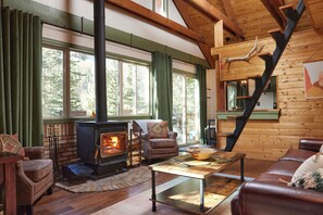 A cozy living room with a wood-burning stove, leather furniture, and a large window with curtains.