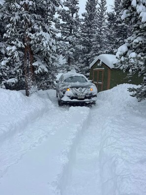 A car navigating a snowy driveway with a house in the background.