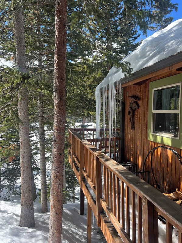 A wooden cabin with a deck, surrounded by trees and covered in snow.