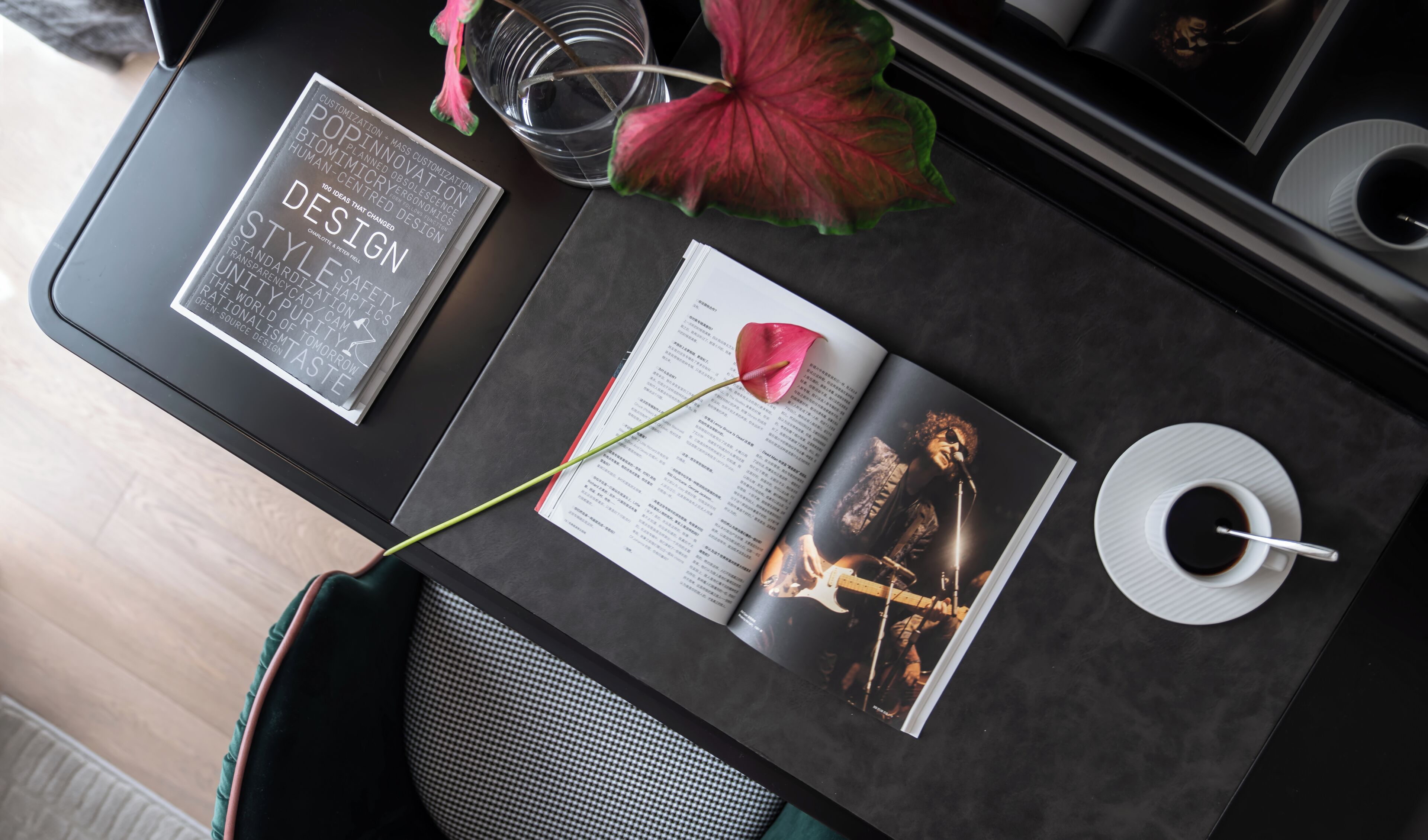 Uma mesa com um livro, uma revista, uma xícara de café e uma flor.