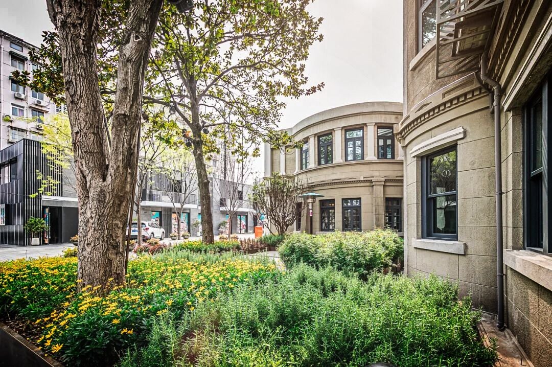 A courtyard with mature trees, a curved building, and a well-maintained garden.