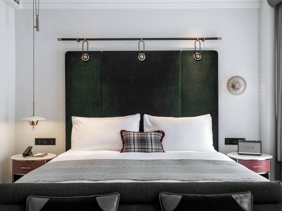 Una habitación de hotel moderna con una cama grande, una mesita de noche con lámpara, radio y toma de corriente.