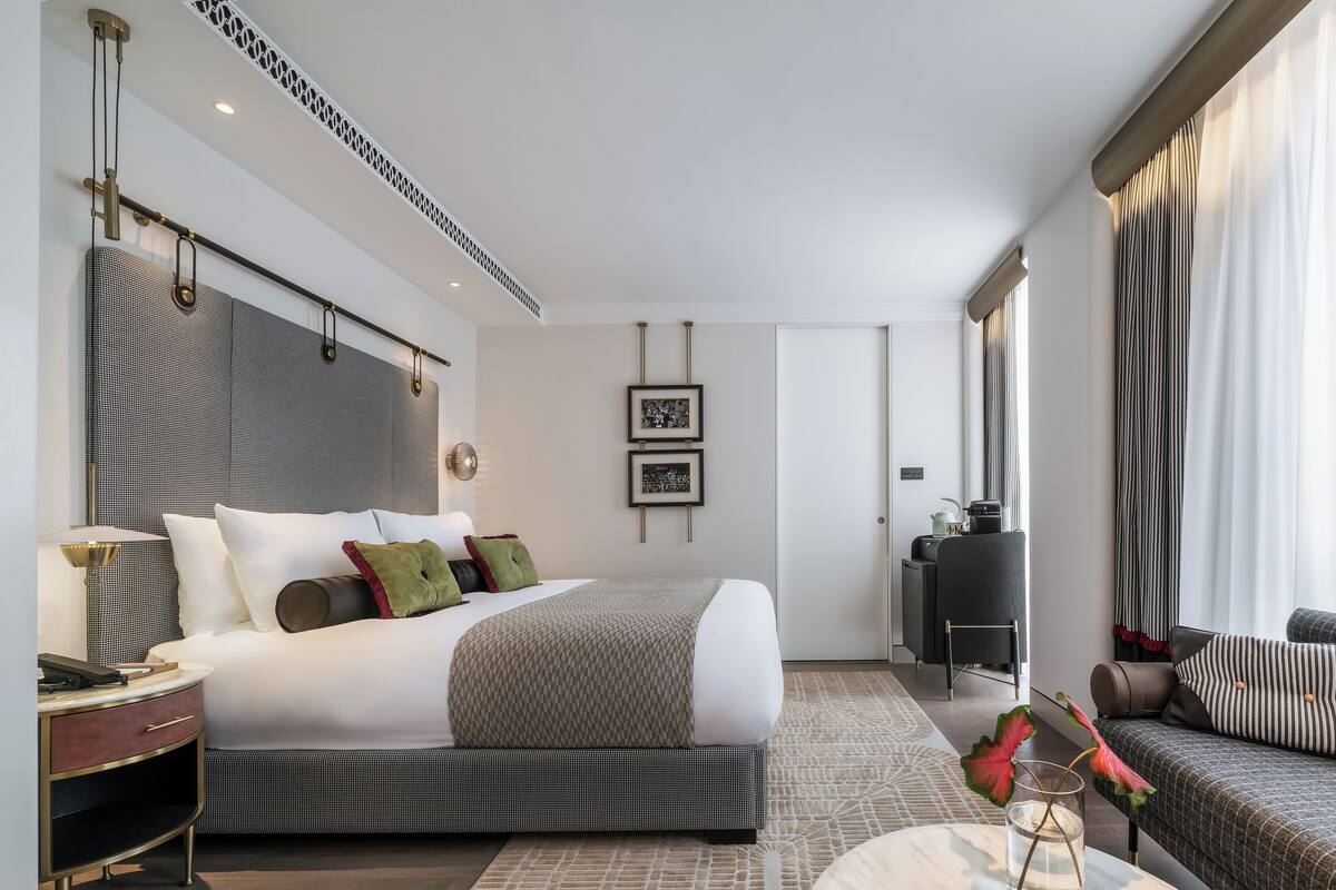 A modern hotel room with a large bed, a sofa, a desk, and a large window with curtains.