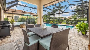 A covered patio with a pool, wicker furniture, and a grill area. - 12894 Epping Way (Fort Myers)
