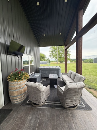 An outdoor patio with a sofa, chairs, a table, and a barrel planter with flowers.. Relax Enjoy Country Living with Hot Tub