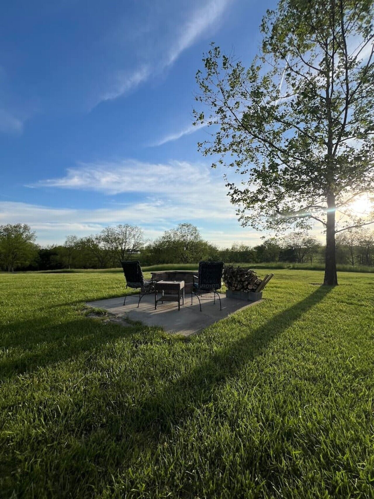 Un espace extérieur aménagé avec une table et des chaises, entouré de pelouse et d’arbres, sous un ciel dégagé.
