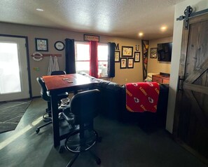 Quarto com uma mesa de madeira, cadeiras de escritório pretas, um cobertor vermelho e quadros nas paredes.