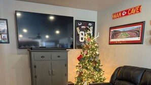 A living room with a flat-screen TV, a Christmas tree, a couch, and a small stool. - Relax Enjoy Country Living-Hot Tub & Seasonal Pool (New Franklin)