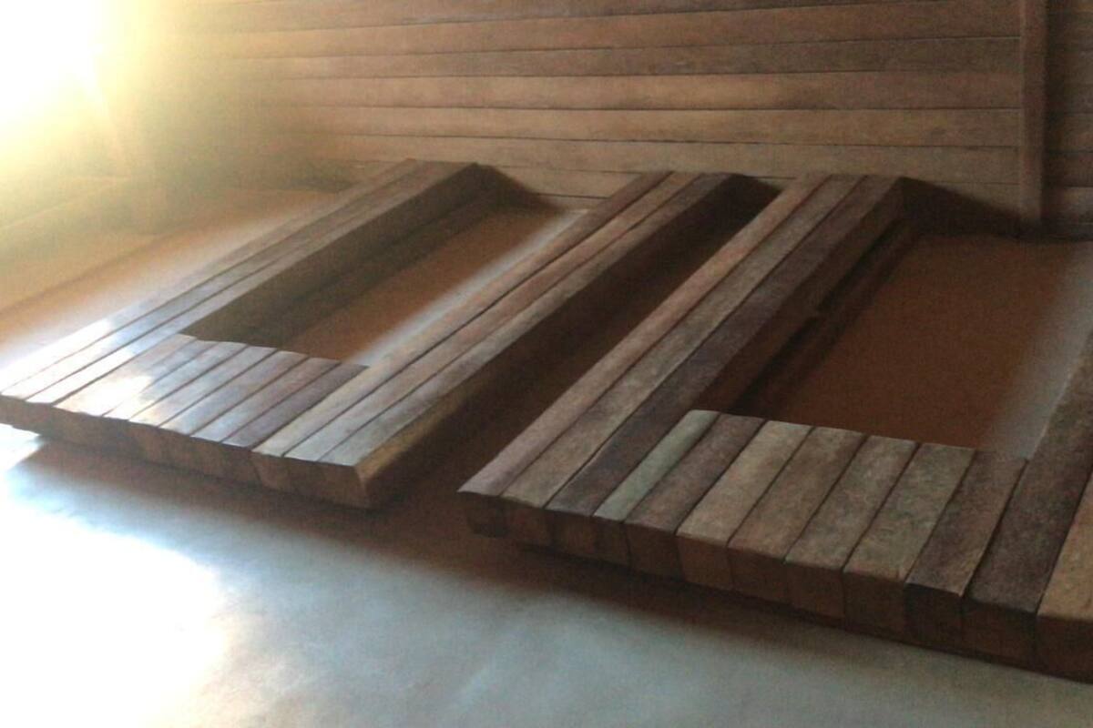 Two wooden benches with a slatted design, placed on a wooden floor against a wall with horizontal wooden planks.