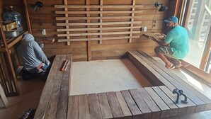 A room with a wooden bench, a table, and a person working on a wooden structure.