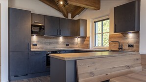 A modern kitchen with dark cabinetry, a wooden island, and built-in appliances. - Superior Ferienhaus # 5D mit Sauna (Uttendorf)
