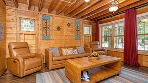 A wooden interior with a sofa, two leather chairs, a coffee table, and a window with curtains. - Dollybrook 1: Dreamy Den | Hot Tub & Pool (Fennville)