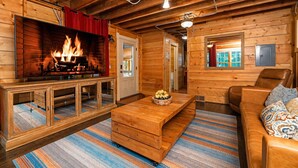 A cozy cabin interior with a fireplace, wooden furniture, and a window with a view. - Dollybrook 1: Dreamy Den | Hot Tub & Pool (Fennville)