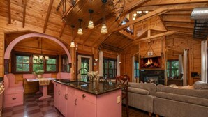 A log cabin interior with a pink kitchen island, a fireplace, and a sofa.