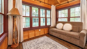 A cozy room with wooden walls, a brown sofa with cushions, a lamp, and large windows.
