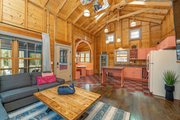 A wooden cabin interior with a sofa, dining table, kitchen area, and large windows. - Dollybrook 4: Bubblegum Bungalow | Pool (Fennville)
