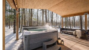 Una vasca idromassaggio in un'area esterna coperta con un pavimento in legno, circondata da alberi innevati.