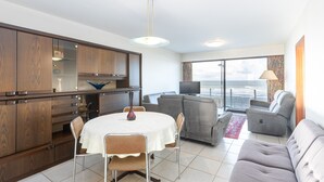 Una sala de estar moderna con comedor, sofás grises, televisor y vista al mar.