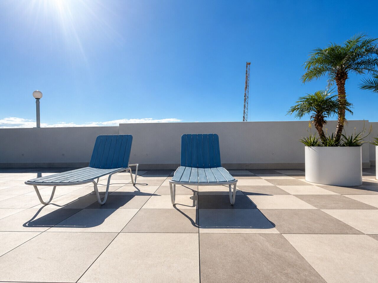 Dos sillones de descanso en un patio con suelo de baldosas, cielo despejado y una palmera.