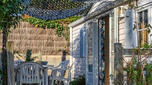 A wooden deck with a table and chairs, a thatched wall, and a house with blue shutters. - La Spatule by Interhome (Carnac)