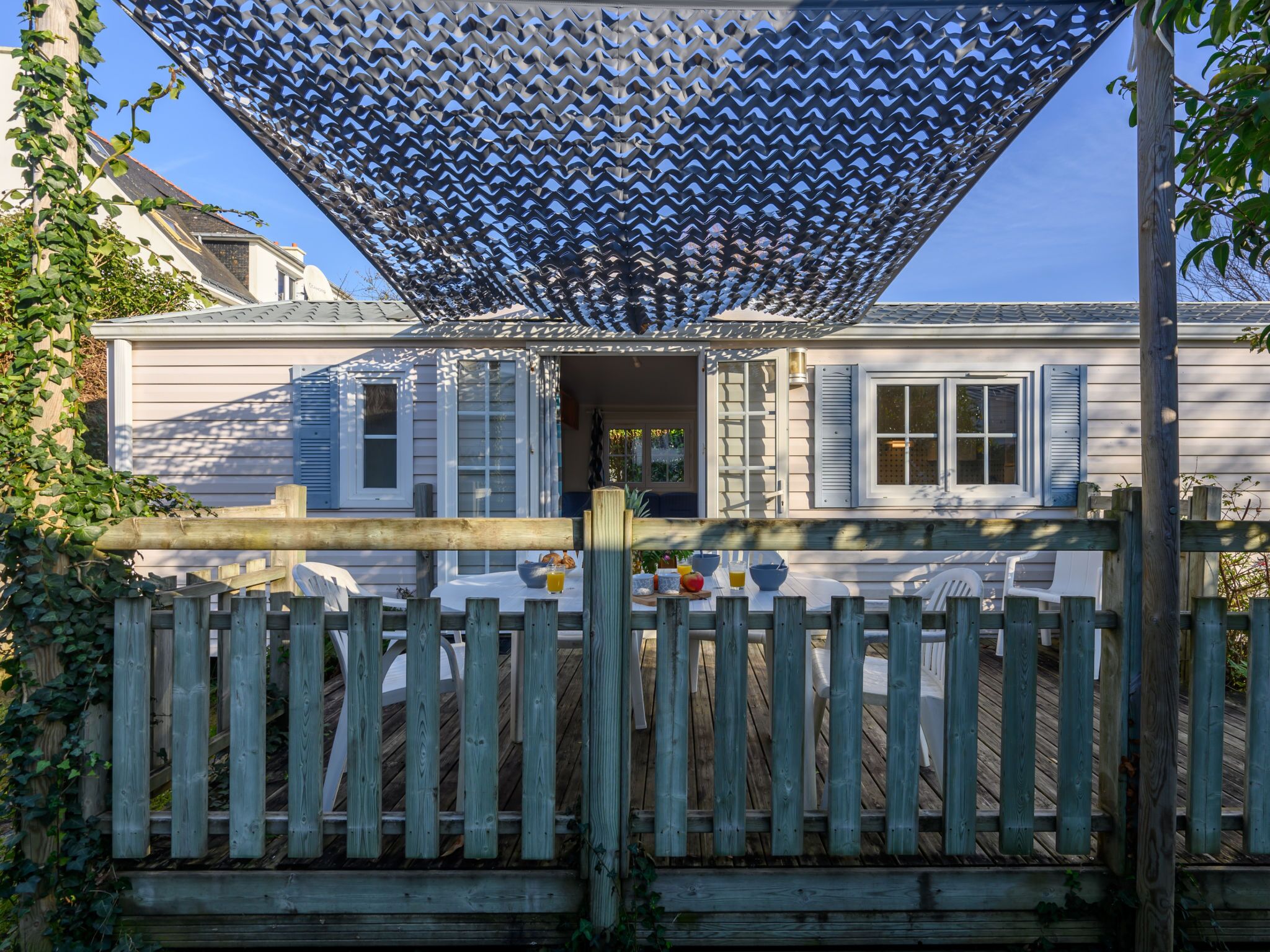Een huis met een overdekte patio, een houten omheining en een tafel met buitenmeubels.