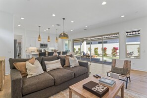 A modern living room with a sofa, coffee table, and a view of a pool and garden. - PGA West retreat w/ pool, hot tub & mountain views (La Quinta)
