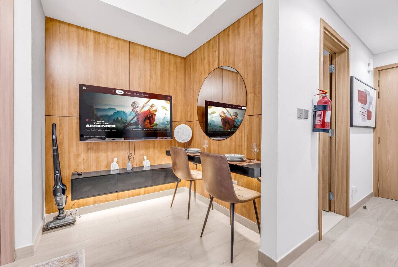 Un comedor moderno con una pared de madera, un televisor de pantalla plana grande, un espejo redondo y un extintor.
