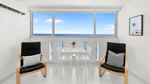 A room with a large window overlooking the sea, two chairs, a table, and a framed picture on the wall. - Chic Studio in Condado | Beach at Your Doorstep (San Juan)