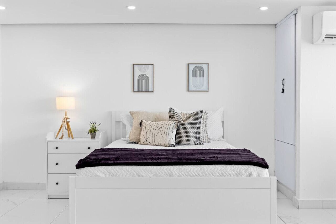 A modern bedroom with a white bed, a bedside table with a lamp, and two framed pictures on the wall.