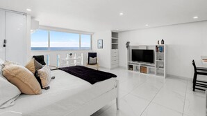A modern bedroom with a large bed, a TV, and a view of the sea. - Chic Studio in Condado | Beach at Your Doorstep (San Juan)