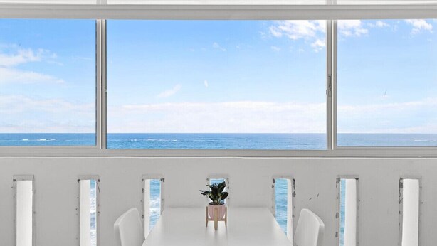 A room with a large window overlooking the sea, a white table, and a potted plant. - Chic Studio in Condado | Beach at Your Doorstep (San Juan)
