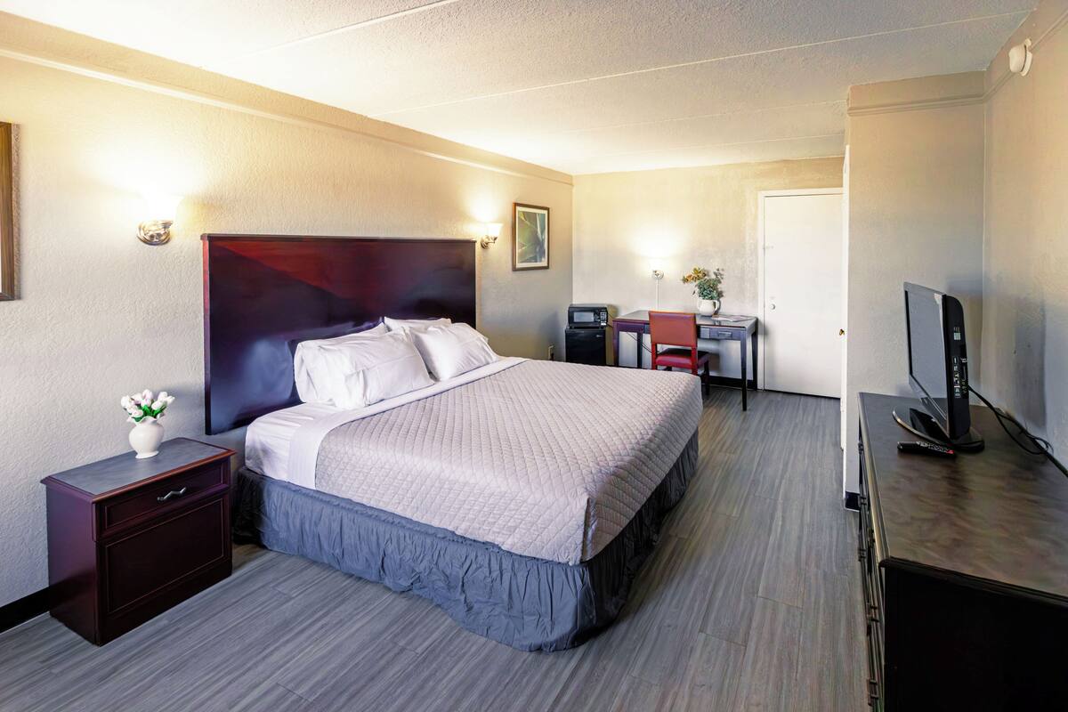 Et hotelværelse med seng, skrivebord, fjernsyn og et natbord.